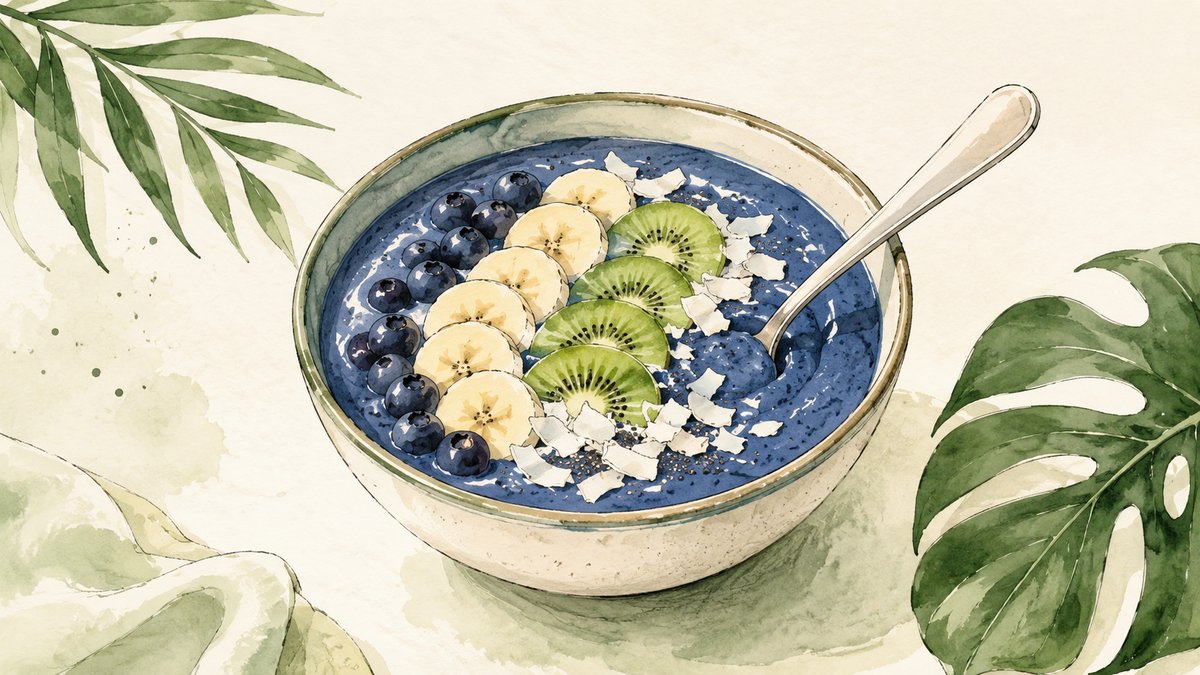 A thick blue spirulina smoothie bowl topped with sliced fruit and coconut flakes